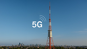 Roter Sendeturm mit 5G-Symbol vor blauem Himmel Symbolisches Bild für 5G-Funktechnologie: Sendeturm mit 5G-Logo und Stadtsilhouette im Hintergrund.