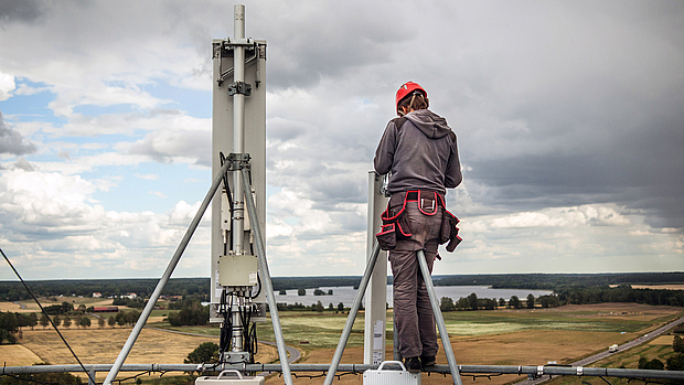 Network Realization & Implementation – End-to-End Deployment A technician working on a communication tower with a rural landscape in the background, representing LS telcom’s expertise in network rollout, system integration, and commissioning.