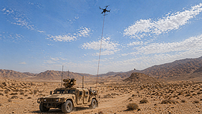Tethered drone above a military vehicle in desert terrain during airborne monitoring operations.