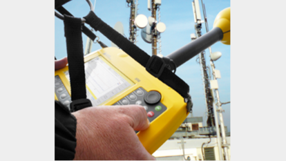 Measuring Electromagnetic Radiation with Handheld Device Close-up of a person operating a yellow handheld electromagnetic field meter in front of broadcast antennas, representing LS telcom’s radiation hazard assessment and public awareness services.