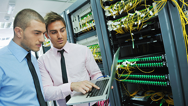 Network Operation Support – Training & Troubleshooting Assistance Two IT professionals analyzing a laptop screen in front of a server rack, representing LS telcom’s support services for network operations, troubleshooting, and training.